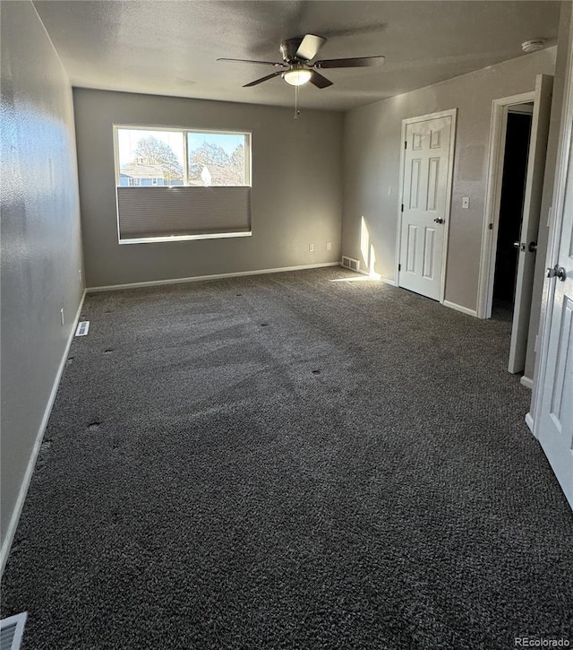 spare room featuring visible vents, baseboards, dark colored carpet, and a ceiling fan