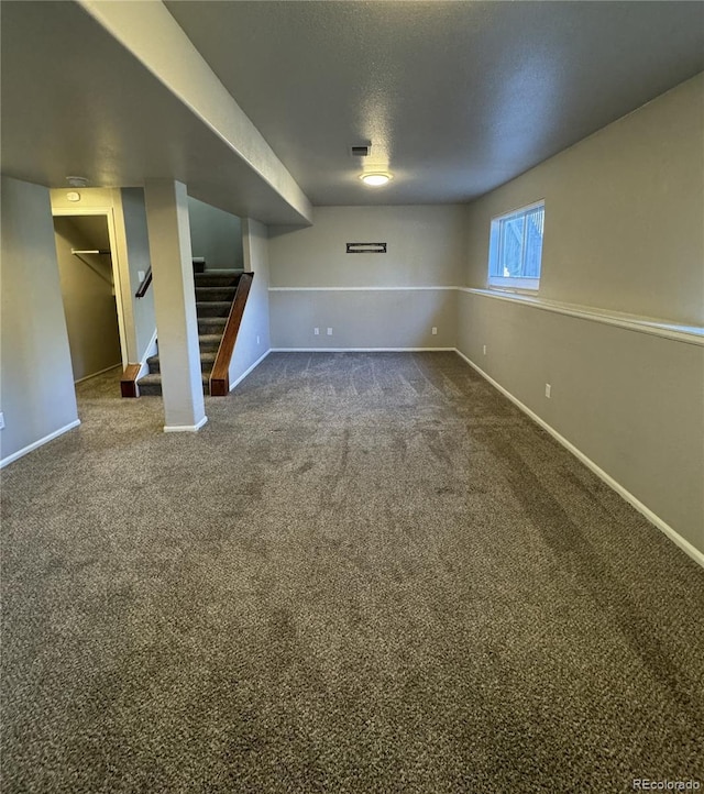 below grade area featuring baseboards, stairs, dark carpet, and a textured ceiling