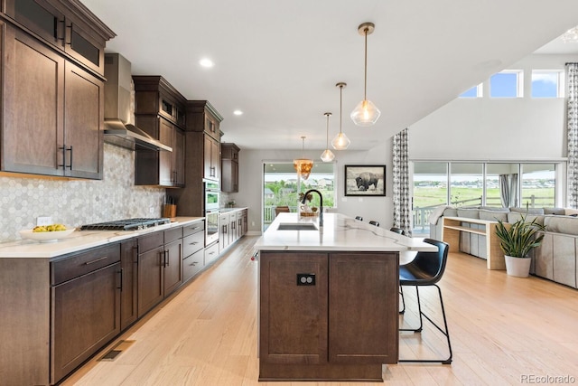 423 Rogers Way, Castle Rock, CO 80104 - kitchen featuring wall chimney exhaust hood, open floor plan, light wood-type flooring, dark brown cabinets, and a kitchen bar