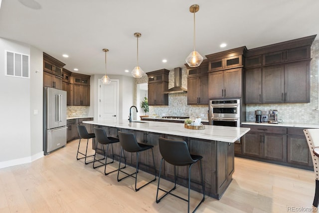 423 Rogers Way, Castle Rock, CO 80104 - kitchen featuring appliances with stainless steel finishes, wall chimney range hood, decorative backsplash, light wood-type flooring, and dark brown cabinets