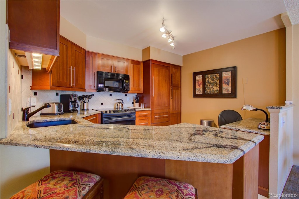 kitchen featuring light stone counters, a sink, black microwave, electric range, and a peninsula