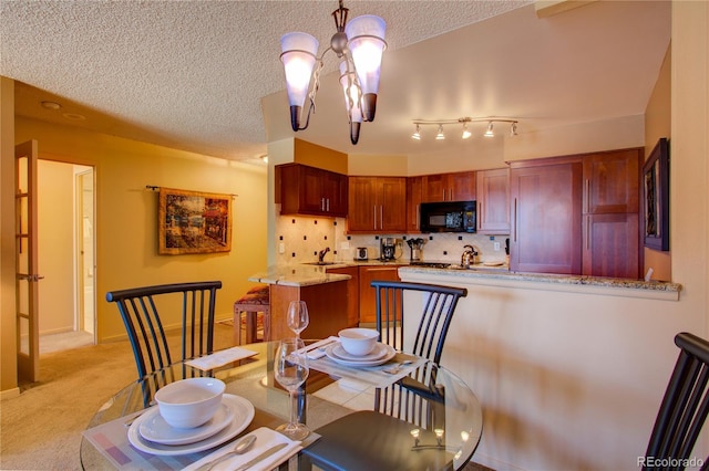 carpeted dining room with sink, a textured ceiling, an inviting chandelier, and track lighting