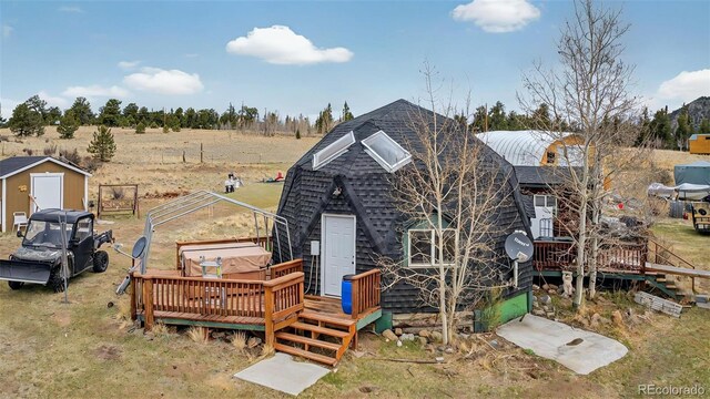 rear view of property featuring a wooden deck, roof with shingles, a storage shed, a view of rural / pastoral area, and an outdoor structure