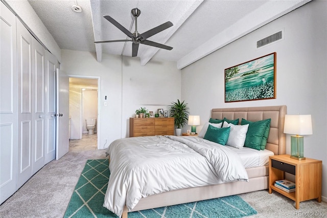 carpeted bedroom featuring a textured ceiling, ceiling fan, ensuite bathroom, visible vents, and beam ceiling