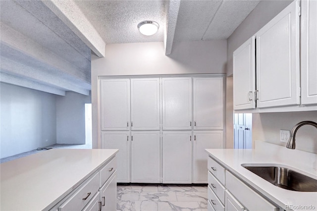 kitchen with marble finish floor, light countertops, a textured ceiling, white cabinetry, and a sink