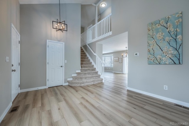 entryway with visible vents, stairs, a high ceiling, an inviting chandelier, and wood finished floors