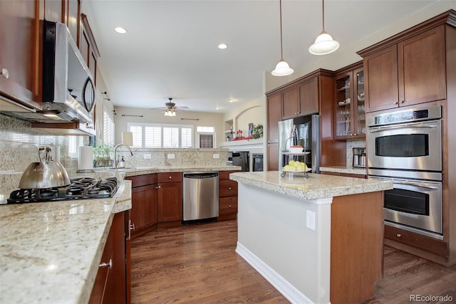 kitchen featuring appliances with stainless steel finishes, a center island, ceiling fan, and dark wood-type flooring