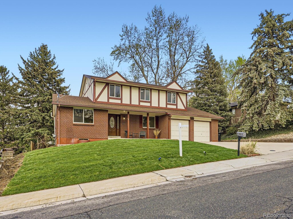 6768 Vivian St, Arvada, CO 80004 - tudor home with concrete driveway, brick siding, a front yard, a garage, and covered porch