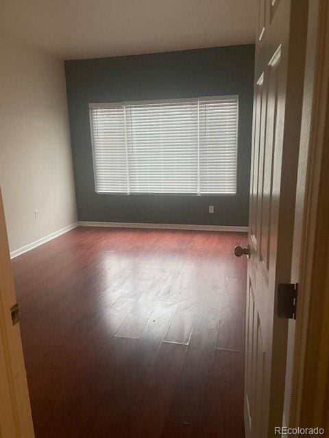 empty room with dark wood-type flooring and baseboards