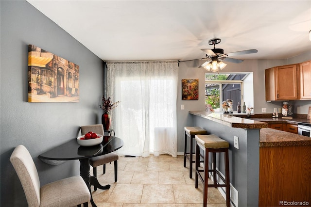 9713 W Chatfield Ave Unit F, Littleton, CO 80128 - kitchen featuring a kitchen bar, a peninsula, ceiling fan, brown cabinets, and light tile patterned flooring