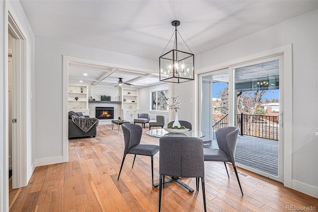 dining space with light hardwood / wood-style flooring, built in features, coffered ceiling, a brick fireplace, and beamed ceiling