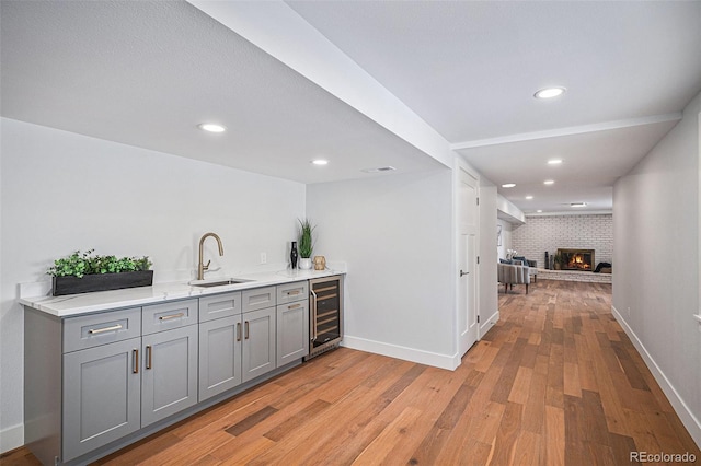 bar featuring wine cooler, sink, a brick fireplace, and gray cabinetry