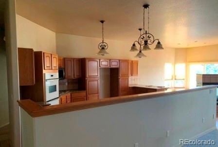 kitchen with pendant lighting, kitchen peninsula, oven, and an inviting chandelier