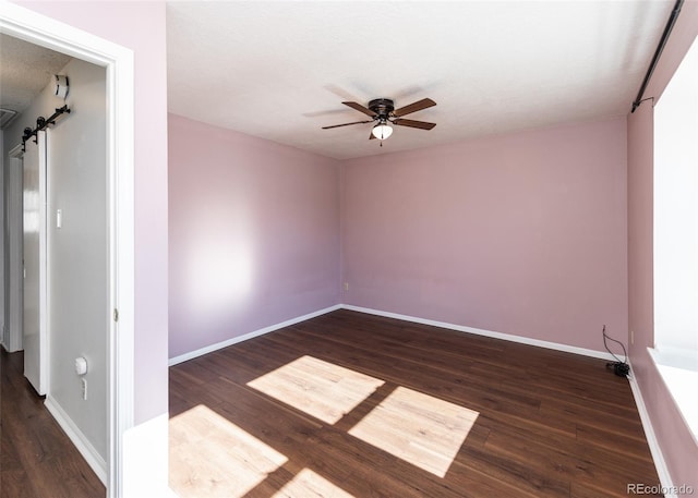 unfurnished room featuring a textured ceiling, ceiling fan, a barn door, and dark wood-type flooring