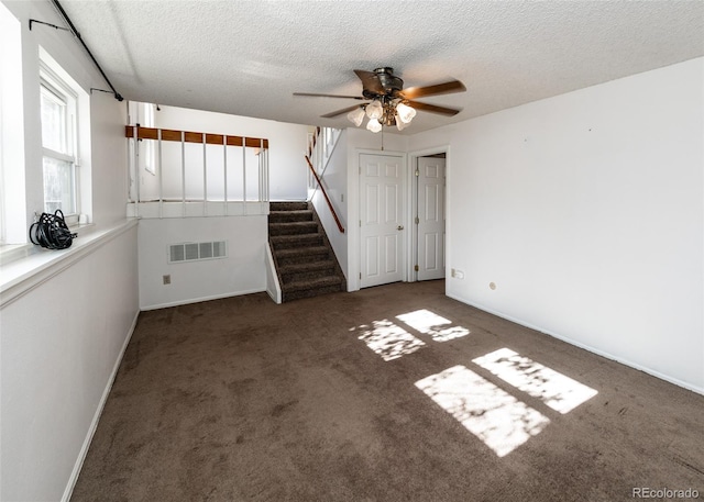 unfurnished living room featuring ceiling fan, dark carpet, and a textured ceiling