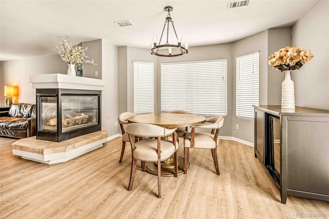 dining area with an inviting chandelier, light hardwood / wood-style flooring, and a multi sided fireplace