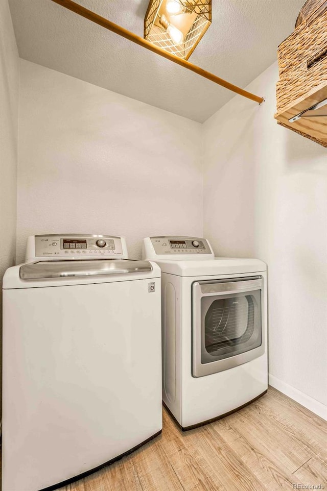 laundry room with a textured ceiling, washing machine and clothes dryer, and light wood-type flooring