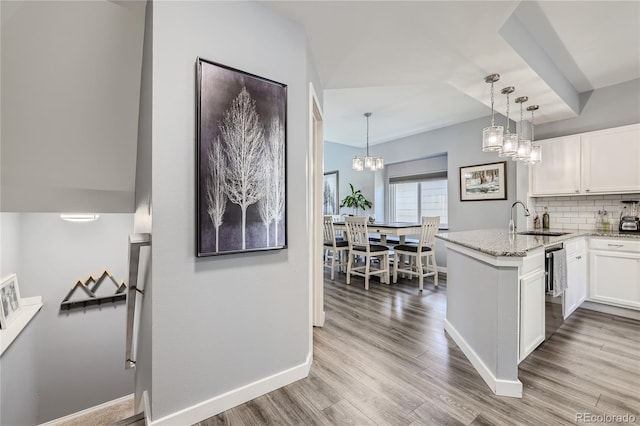 kitchen with kitchen peninsula, decorative backsplash, white cabinets, light wood-type flooring, and pendant lighting