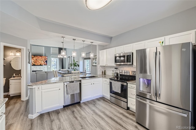 kitchen featuring light hardwood / wood-style flooring, hanging light fixtures, kitchen peninsula, white cabinets, and appliances with stainless steel finishes