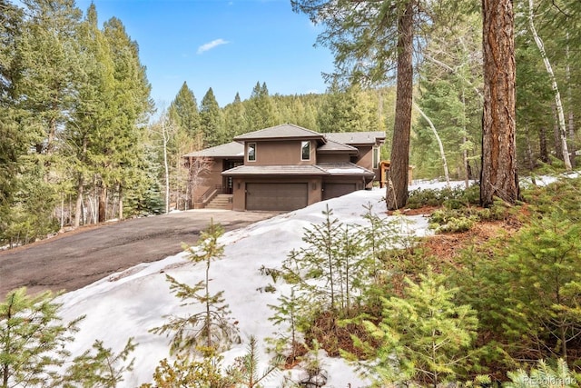 view of front of property with stucco siding, driveway, a forest view, and a garage