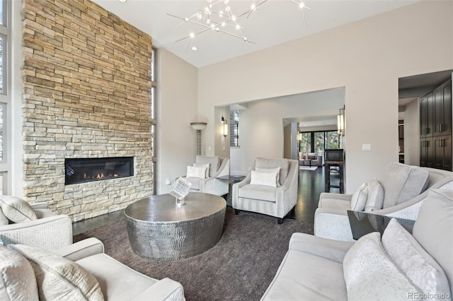 living room with a stone fireplace, a high ceiling, wood finished floors, and an inviting chandelier