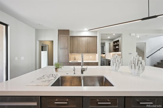 kitchen with a sink, tasteful backsplash, dark brown cabinets, recessed lighting, and light stone counters