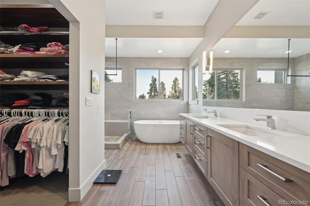 full bathroom featuring a soaking tub, a sink, double vanity, a spacious closet, and wood finished floors