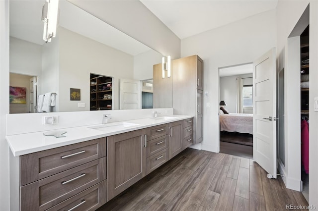 ensuite bathroom with a spacious closet, wood finished floors, a sink, and double vanity