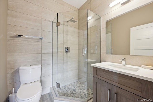full bath featuring a shower stall, toilet, vanity, and tile walls