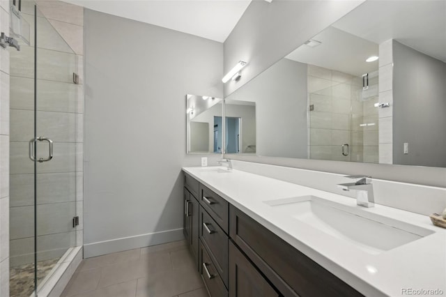 full bathroom featuring a shower stall, tile patterned flooring, double vanity, a sink, and baseboards