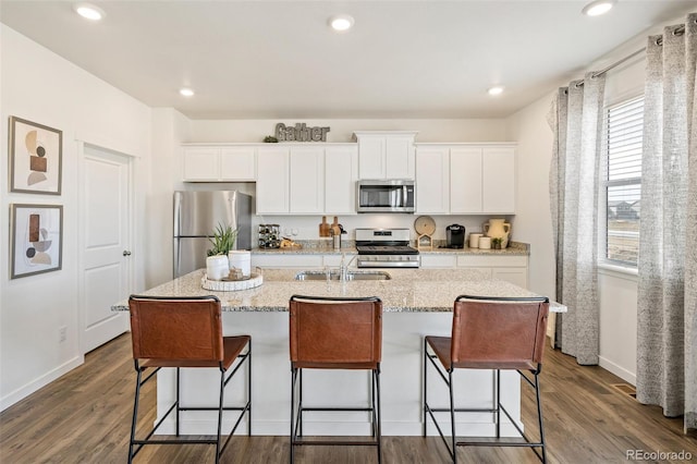 kitchen with dark wood-type flooring, white cabinetry, stainless steel appliances, and an island with sink