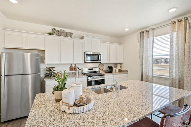 kitchen featuring light stone countertops, appliances with stainless steel finishes, and a kitchen island with sink