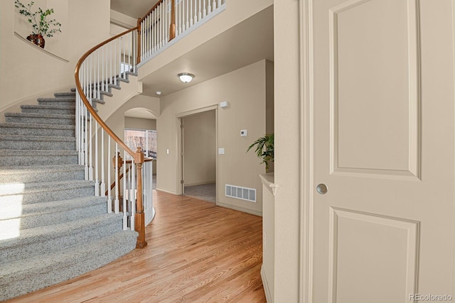 stairs with arched walkways, a high ceiling, wood finished floors, visible vents, and baseboards