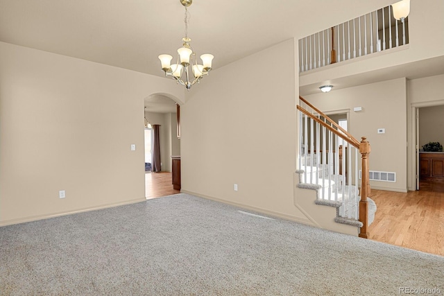 spare room featuring visible vents, arched walkways, stairs, carpet floors, and a notable chandelier