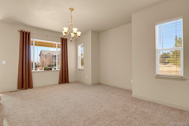 spare room featuring carpet floors, an inviting chandelier, plenty of natural light, and baseboards