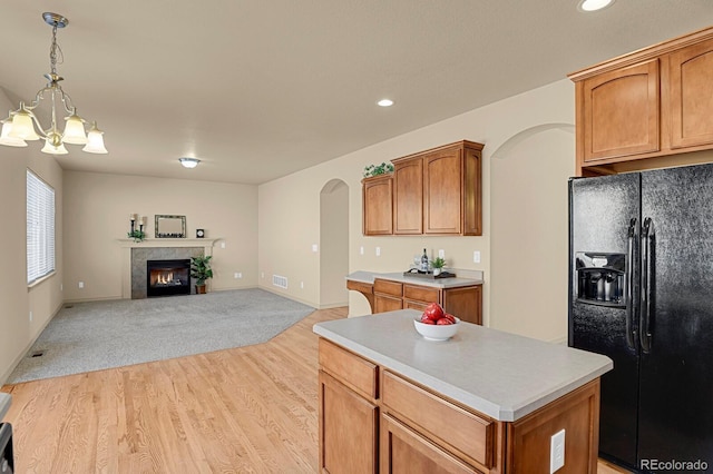 kitchen with arched walkways, a fireplace, black fridge with ice dispenser, open floor plan, and light countertops