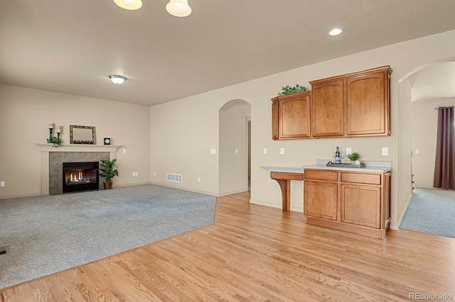 kitchen featuring arched walkways, a tile fireplace, visible vents, light countertops, and light wood finished floors