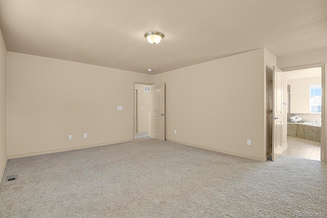 empty room featuring a textured ceiling, baseboards, and light colored carpet