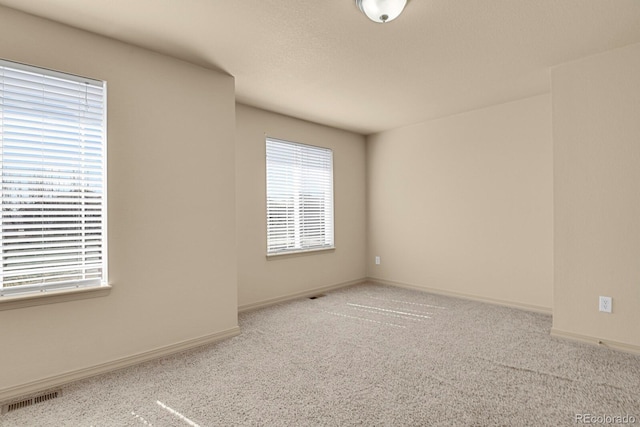 spare room featuring carpet floors, visible vents, and baseboards