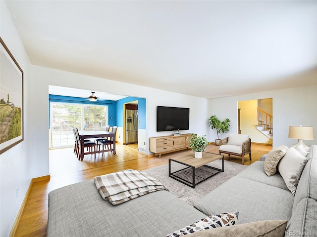 living room featuring stairs, light wood-type flooring, and baseboards