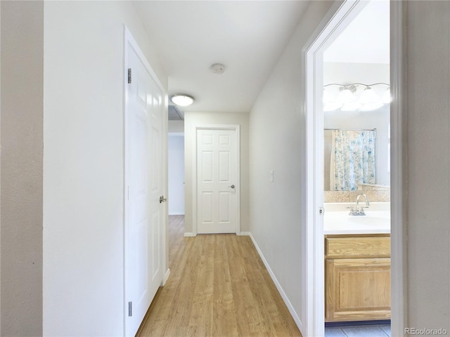 corridor with light wood-type flooring, baseboards, and a sink