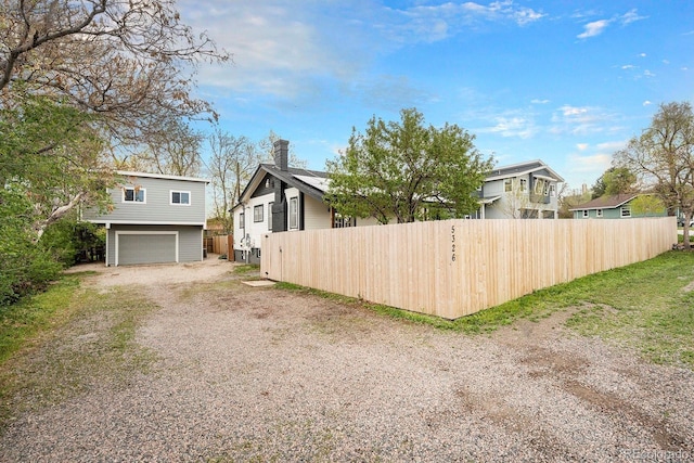 view of side of home featuring a garage, dirt driveway, fence, and a chimney