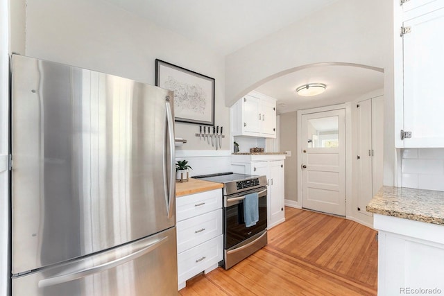 kitchen with white cabinets, light wood-style floors, arched walkways, stainless steel appliances, and backsplash