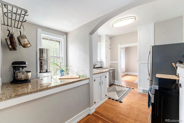 kitchen featuring stainless steel dishwasher, arched walkways, stove, and light wood-style floors