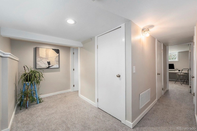 hallway with baseboards, light colored carpet, and visible vents