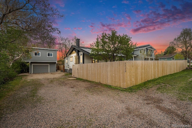 exterior space with fence, dirt driveway, a chimney, and a garage