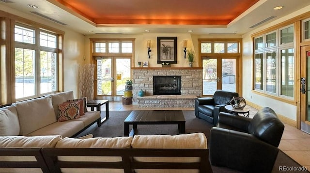 living room with tile patterned flooring, a stone fireplace, french doors, and a tray ceiling