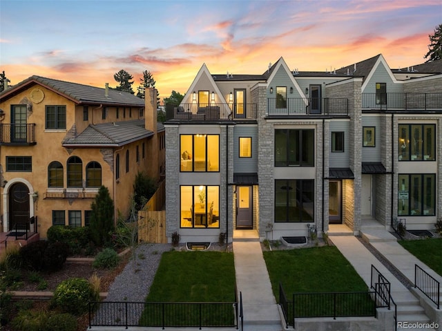 back house at dusk featuring a yard and a balcony