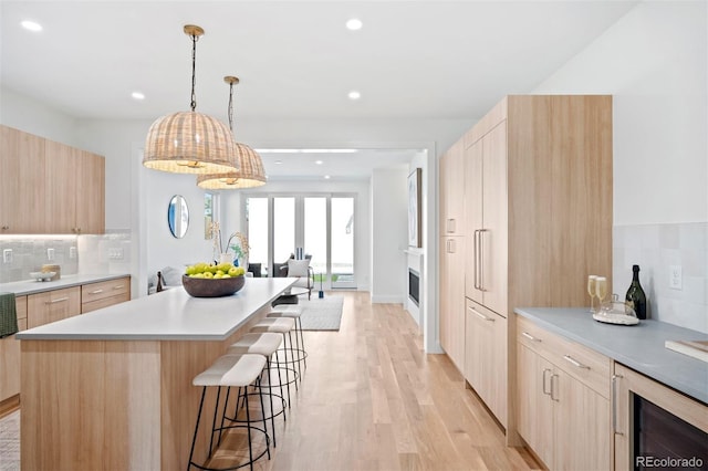 kitchen with light brown cabinets, hanging light fixtures, light hardwood / wood-style flooring, tasteful backsplash, and beverage cooler