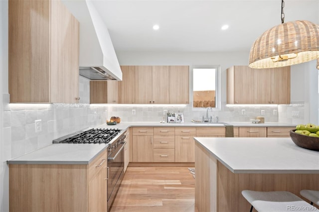 kitchen with light brown cabinetry, light wood-type flooring, high end stove, sink, and hanging light fixtures